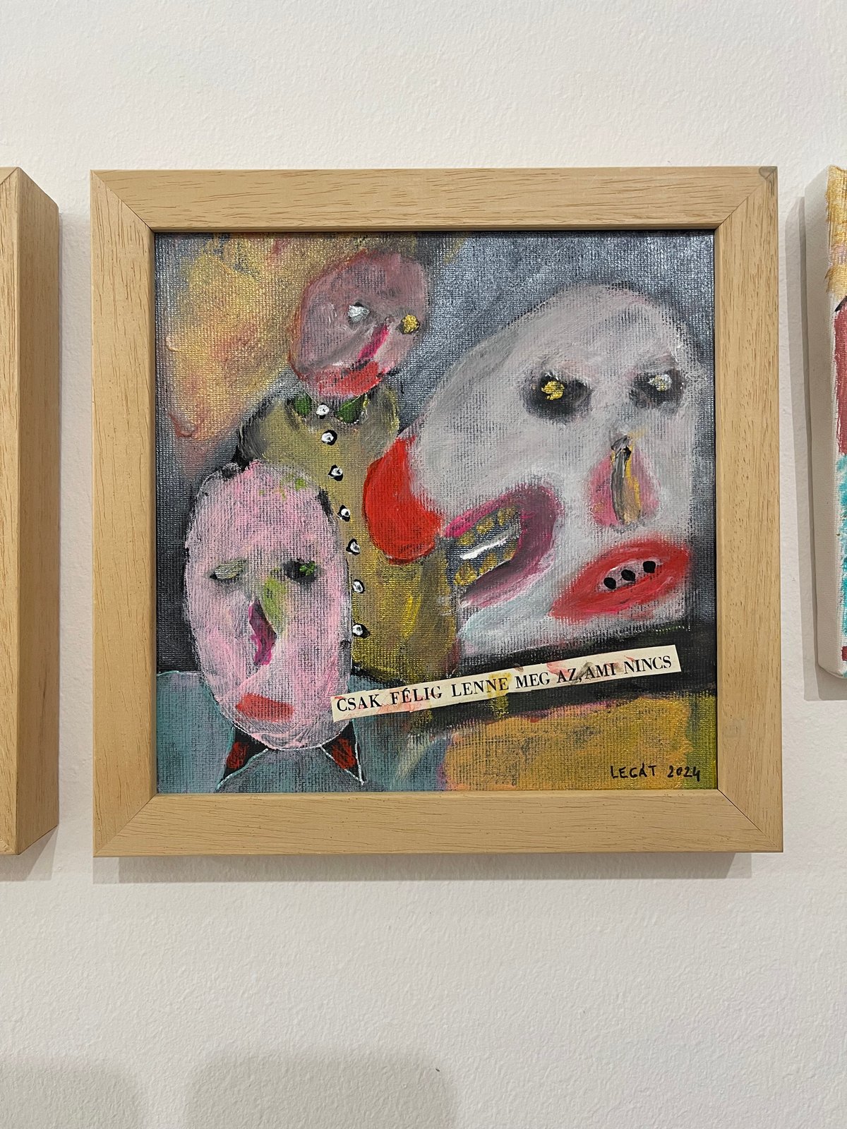 Legát Tibor’s Csak félig lenne meg, ami nincs, a grey and pink expressive painting with three distorted faces and a text strip